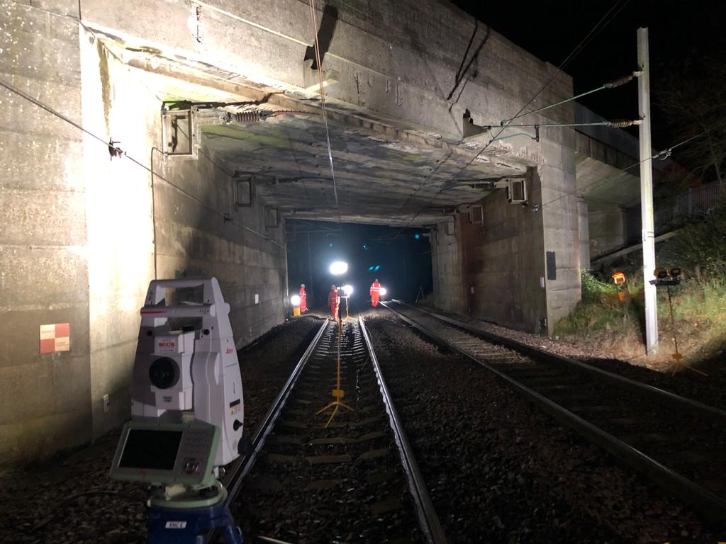 Night time total station working on rail looking under a bridge
