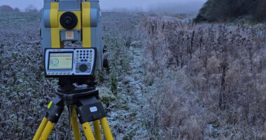 A Geomax Total Station on a tripod in an icy field with the Encompass Surveys logo in the corner